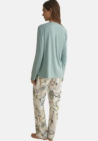 Haut à manches longues bleu clair associé à un pantalon de pyjama crème à motifs présentant des oiseaux colorés et des branches, fabriqué en tissu doux et léger.