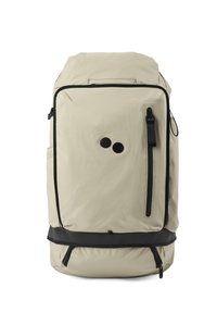 Beiger Stoff-Rucksack mit schwarzen Akzenten, ausgestattet mit einer vorderen Reißverschlusstasche, runder Form und doppeltem kreisförmigem Emblem auf der Vorderseite.