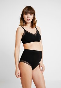 Black bra and high-waisted briefs set. Smooth fabric with sheer lace accents. Bra features adjustable straps and a subtle twist detail.