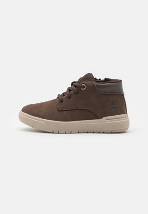 Baskets mid-top marron avec semelle beige, lacets à l'avant, col rembourré et logo arbre embossé sur le côté du talon.