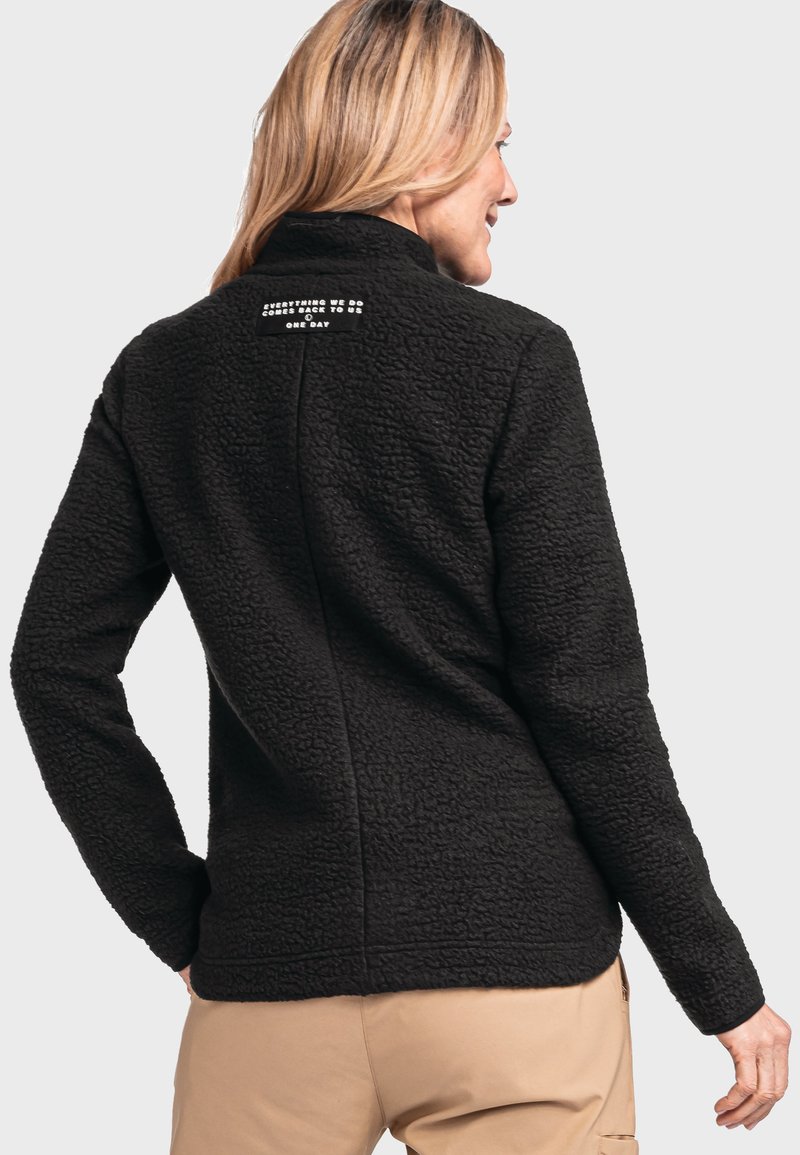Giacca di fleece nera con finitura texturizzata, colletto alto e etichetta stampata sul retro. Presenta maniche lunghe e un orlo curvo.