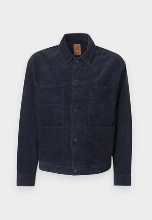 Tamsiai mėlynas korduro audinio švarkas su apykakle, užsegamas sagomis, dvi kišenės priekyje. Tekstūruotas audinys, tiesus kirpimas, minimalus dizaino detalių.