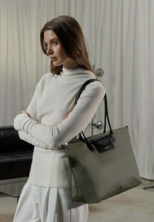 Sac fourre-tout kaki avec des accents en cuir noir, présentant une forme structurée et deux longues poignées. Le sac a une texture lisse et un design minimaliste.
