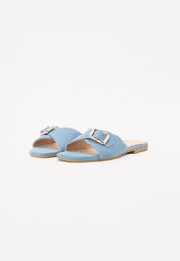 Blå denim sko med bred rem og et stort spænde. Flad sål med en subtil tekstur og åben tå design.
