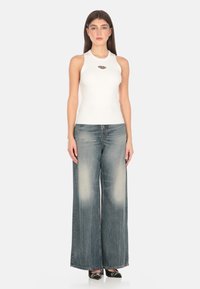 Top in cotone bianco a coste con dettagli a foro rotondo, abbinato a jeans a gamba larga in blu sbiadito e scarpe nere con tacco.
