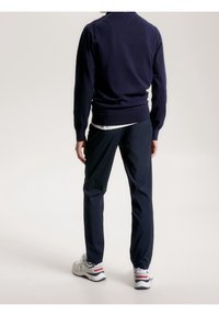 Suéter azul marino con dobladillo y puños acanalados, combinado con pantalones azul marino a juego. Zapatillas grises con acentos en rojo y azul.