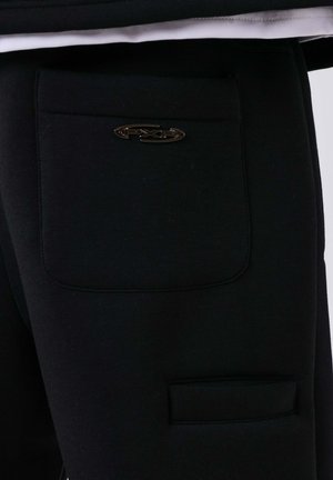 Pantalons noirs en tissu doux avec une texture lisse. Dotés de deux poches et d'un accent de logo métallique sur la poche arrière.