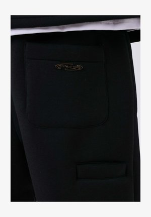 Pantalons noirs en tissu doux avec une texture lisse. Dotés de deux poches et d'un accent de logo métallique sur la poche arrière.