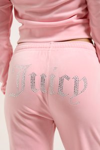 Rozā velūra sporta bikses ar rhinestone "Juicy" logo aizmugurē. Elastīga josta ar gludu tekstūru un pieguļošu dizainu.