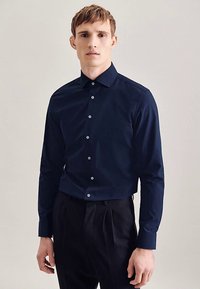 Camicia a maniche lunghe blu navy con colletto appuntito, chiusura frontale con bottoni e tessuto liscio e leggermente strutturato. Design a taglio sartoriale.