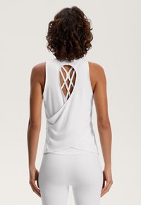 Top bianco senza maniche con un design a schiena intrecciata e dettaglio incrociato. Tessuto morbido con una texture liscia e orlo curvo.