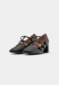 Black flat shoes with a pointed toe and triangular block heel. Features crisscross straps and gold-tone hardware accents. Satin finish.