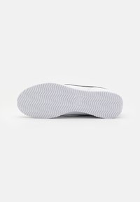 White athletic shoe sole with zigzag tread pattern, featuring a small Nike logo. Upper part not visible.