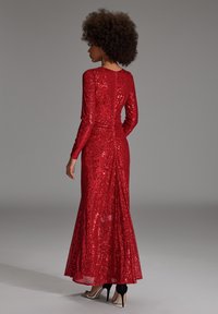 Rode pailletten avondjurk met lange mouwen, aansluitend lijfje, uitlopende rok en een split aan de achterkant, met een gladde textuur en glanzende metalen accenten.