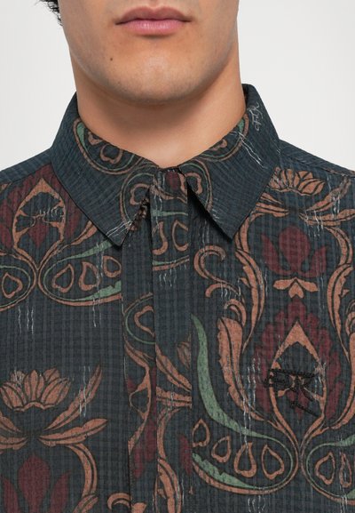 Shirt featuring a dark patterned fabric with floral motifs in green, red, and beige, structured collar, and button-up front.