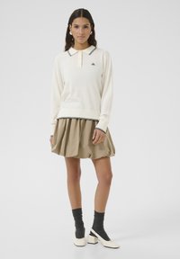 Cream long-sleeve polo sweater with black trim, paired with a beige puff skirt. Worn with gray socks and white block-heeled shoes.