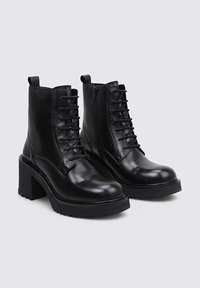 Bottines en cuir noir avec un talon épais, avant à lacets et fermeture éclair sur le côté. Texture lisse avec une semelle en caoutchouc durable et une languette à l'arrière.