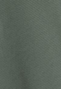 Tessuto verde con texture e finitura liscia, caratterizzato da un sottile motivo di linee fini sulla superficie. Materiale leggero e elasticizzato.