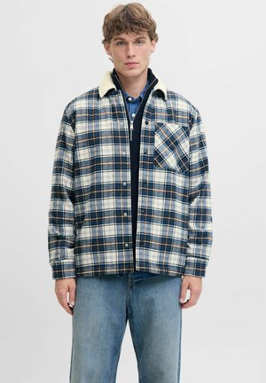 Veste en flanelle à carreaux dans des teintes de bleu, beige et marron. Elle possède un col en sherpa, une poche poitrine et une fermeture à boutons. Tissu doux, coupe décontractée.