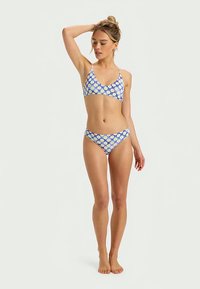 Mėlynos ir baltos spalvų raštuotas bikinio komplektas, kuriame yra liemenėlės tipo viršus su plonais dirželiais ir atitinkamais žemais kelnaitėmis. Glotnus audinys su gėlių raštu.