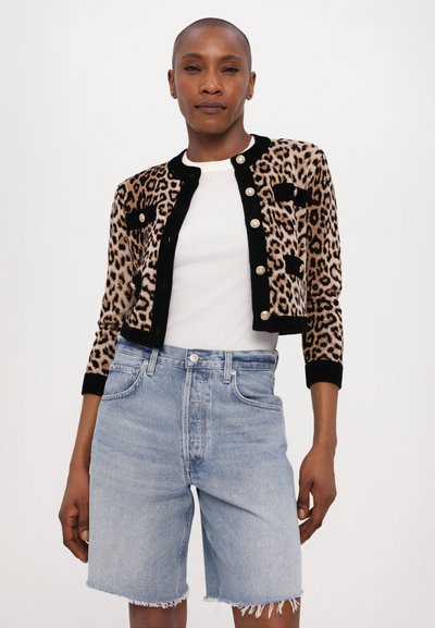 Cardigan cu imprimeu leopard și accente negre, cu mâneci lungi și închideri cu nasturi aurii, asortat cu pantaloni șort din denim de culoare albastru deschis, cu marginile desfăcute.