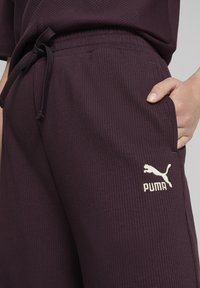 Donkerpaarse geribbelde joggingbroek met een trekkoord in de taille, zijzakken en een wit Puma-logo op de linkertas.