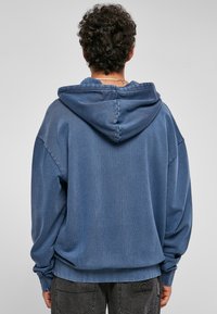 Felpa con cappuccio blu in un tessuto testurizzato, vestibilità comoda e spalle scese. Sul retro presenta dettagli di cucitura e un logo sottile sull'orlo.