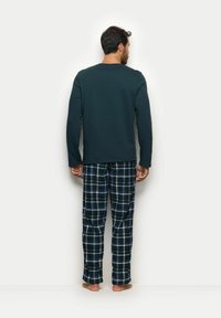 Top de manga larga verde oscuro combinado con pantalones de cuadros azul marino que presentan un patrón a cuadros blanco y verde, hechos de una tela suave y con un ajuste relajado.