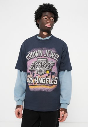 Navy graphic t-shirt with "CROWN JEWEL KINGS LOS ANGELES" print in pink and yellow; layered over light blue long-sleeve shirt; cotton fabric.