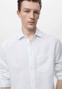 White, long-sleeve linen shirt featuring a button-down collar and a chest pocket, with a relaxed fit and subtle texture.