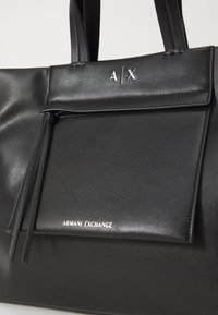 Borsa a tracolla in similpelle nera con tasca frontale a pattina, dettagli in logo argentato e texture liscia. Presenta doppi manici per il trasporto.