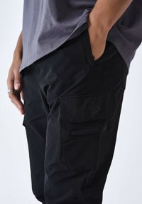 Pantalones cargo negros hechos de tela resistente, con un bolsillo lateral con tapa, un logotipo sutil y un diseño recto.