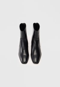 Botas de cuero negras hasta el tobillo con un diseño elegante, punta cuadrada y cierre lateral. Textura suave con una silueta ajustada.