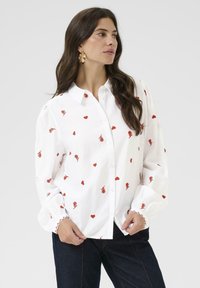 Witte button-up blouse met rode rozen- en hartborduursels. Heeft lange mouwen met geplooide manchetten en een klassieke kraag.