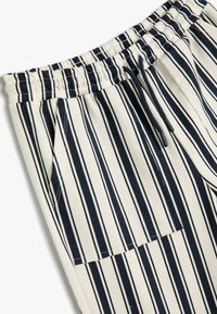 Gestreepte herenbroek in crème met marineblauwe verticale strepen. Bevat een elastische tailleband met een trekkoord en details van zijzakken.