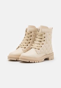 Béžové kožené boty s diamantovým prošíváním, zlatými hřebíky a ladícími tkaničkami. Masivní gumová podrážka zvyšuje stabilitu a přilnavost.