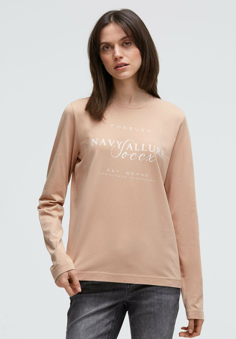 Long-sleeve beige shirt made of soft fabric with printed text "FOREVER NAVY ALLURE" in white. Features a relaxed fit and round neckline.