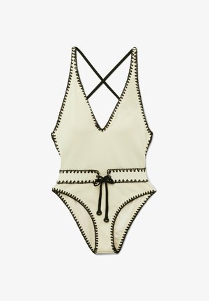 Jednodílné texturované bílé plavky s hlubokým výstřihem do V, černým cikcak lemováním, překříženými ramínky a černým šňůrkovým páskem v pase.