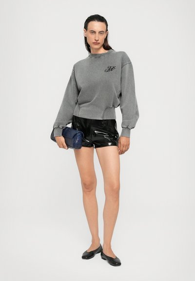Felpa grigia corta con scollatura rotonda e dettaglio con logo, abbinata a pantaloni shorts in vinile neri a vita alta e ballerine nere.