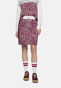 Leopardenmuster Kleid mit tiefburgunderroter Basis, weißen Akzenten und einem Tunnelzug an der Taille; kombiniert mit weißen Socken mit roten Streifen und dunklen Turnschuhen.