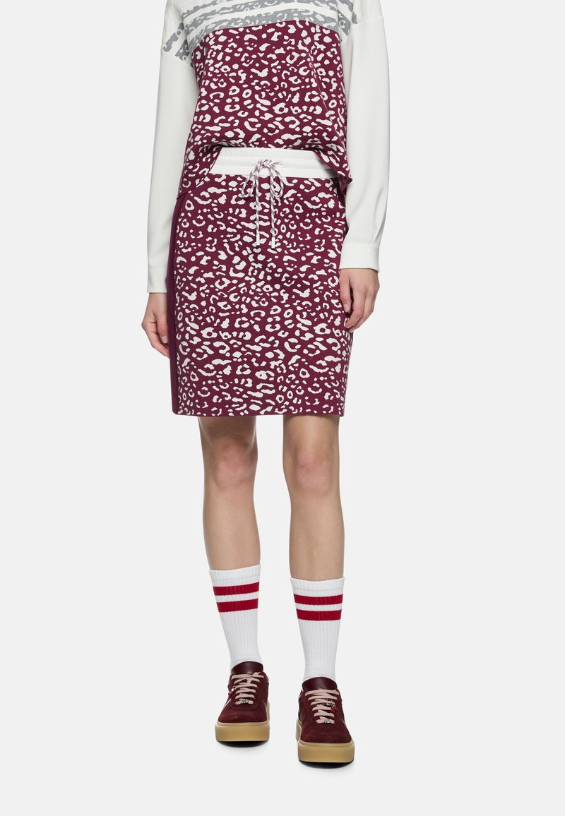 Leopardenmuster Kleid mit tiefburgunderroter Basis, weißen Akzenten und einem Tunnelzug an der Taille; kombiniert mit weißen Socken mit roten Streifen und dunklen Turnschuhen.