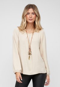 Beige lange mouw top van structuurstof, met een ronde halslijn en elastische manchetten. Verfraaid met een bruine ketting met een ronde hanger.