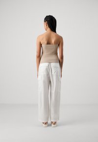 Bežs ribots strapless tops, kas apvienots ar brīviem baltiem kravas biksēm ar sānu kabatām, nēsājot ar rakstainām kurpēm, skatīts no aizmugures.
