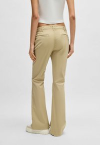 Beige flared trousers with a smooth texture, featuring two back pockets and a mid-rise waistband. Pairing with white platform shoes.