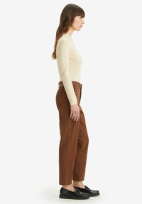 Beige ribbed long-sleeve top, high-waisted brown pants with front pockets, and black loafers with a thick sole, shown from the side.