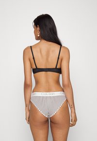 Black bra with adjustable straps, paired with white-and-black striped underwear featuring a branded waistband. Smooth fabric texture.