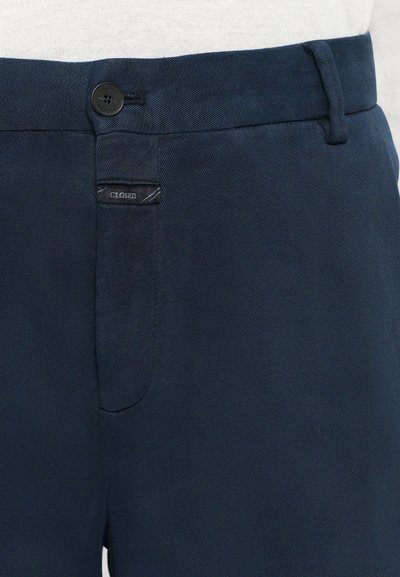 Navy blue woven trousers with a smooth texture, featuring a button fastener, and a stitched logo tag on the left pocket.
