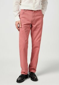 Pantaloni rosa chiaro con taglio dritto, realizzati in cotone, caratterizzati da un classico design a cinque tasche e cuciture a contrasto, abbinati a scarpe nere.