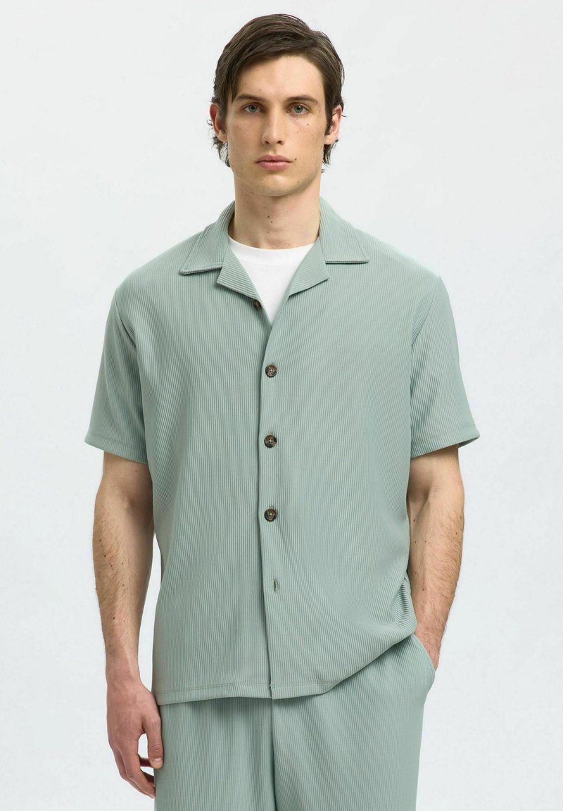 Camicia a maniche corte, verde chiaro, con bottoni, caratterizzata da un design a coste testurizzato e colletto, abbinata a una canottiera bianca e vestibilità comoda.