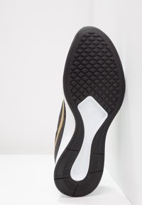 Suela negra de zapato con agarre texturizado, con una entresuela blanca y acentos dorados en la parte superior. Diseño liso y flexible con una forma contorneada.